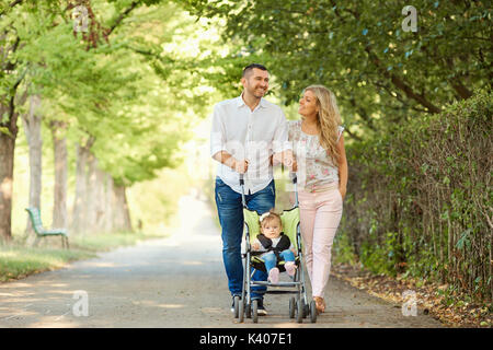 Mother, father and baby in a stroller walking in the park. Stock Photo
