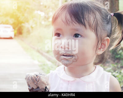 little girl eat ice cream with its mouth smeared with ice cream in park Stock Photo