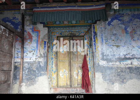 Monks Red Robe Hanging on Door with Tibetan Art Painting at Mu Gompa Monastery, Nepal on Tibetan Border in the Tsum Valley Remote Region Stock Photo