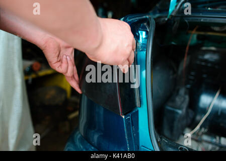 Closeup repairing of an broken blue car in garage by hands of machanic. Stock Photo