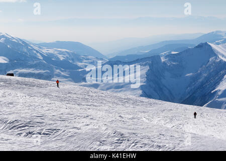 Two skiers downhill on snow off-piste slope and mountains in haze at sun winter day. Caucasus Mountains, Georgia, region Gudauri. Stock Photo