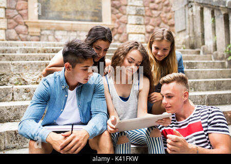Teenage students with tablet sitting on stone steps. Stock Photo
