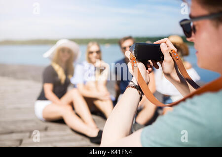 A photo of young man taking a photo of his friends sitting on the pier. Stock Photo