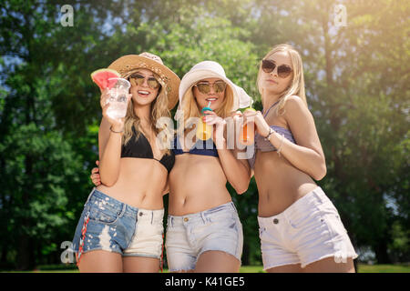 A photo of three beautiful girls standing together with cold drinks and smiling. Stock Photo