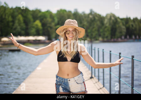 A photo of happy woman in panama hat dancing on the pier and smiling happily. Stock Photo
