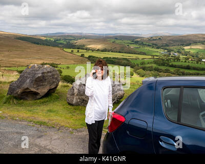 Marure attractive lady trying to phone for help whilst stranded on the moubtainous countryside with a broken down car Stock Photo