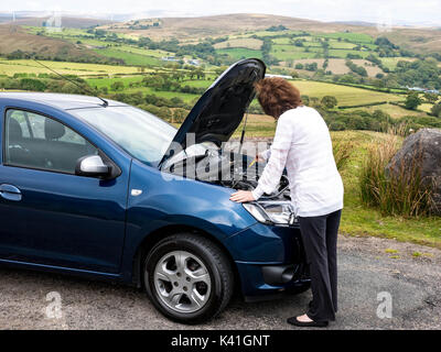 Attrractive mature senior lady checking oild levels to try to find the fault on a broken down car in the middle of nowhere Stock Photo