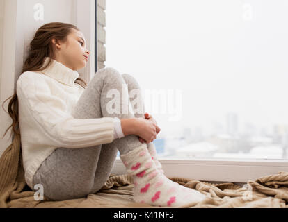 sad girl sitting on sill at home window in winter Stock Photo