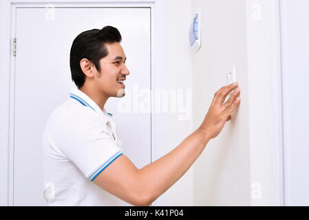 Handsome asian man turning off the light with wall switch in the home Stock Photo