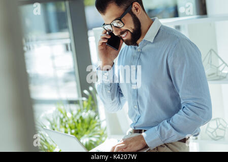 Smiling young man negotiating on the phone at work Stock Photo
