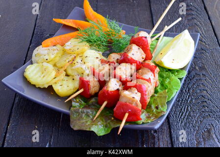 Chicken with paprika on sticks cooked in the oven together with potato on a black plate on a black wooden background. Stock Photo