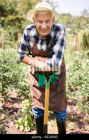 Portrait of senior farmer resting leaning on shovel handle in front of ...