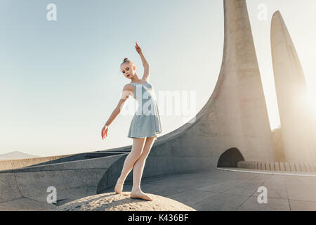 Ballet artist practicing dance moves outdoors. Female dancer standing at a monument practicing dance steps with sun in the backdrop. Stock Photo