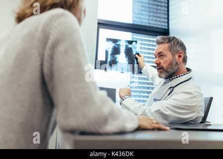 Doctor showing x-ray to his patient in medical office. Physician with patient sitting in examination room and discussing diagnosis of x-ray image. Stock Photo