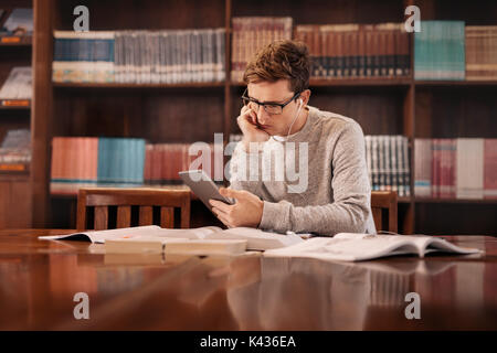 Young student with digital tablet and earphones in the library. college student using tablet pc in the library. Stock Photo