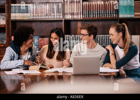 Group of students sitting at table in library and studying together. Happy young friends working on college project. Stock Photo