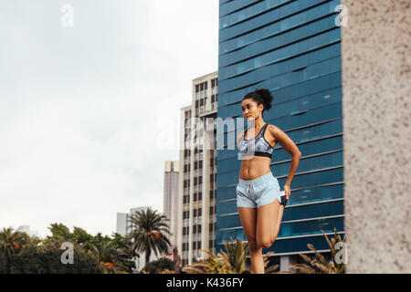 Woman runner doing warm up exercises outdoors. Female athlete exercising outdoors with city buildings in the background. Stock Photo