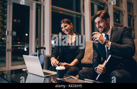 Young businessman and woman waiting at airport lounge and looking at laptop. Business travelers waiting for their flight at airport terminal. Stock Photo