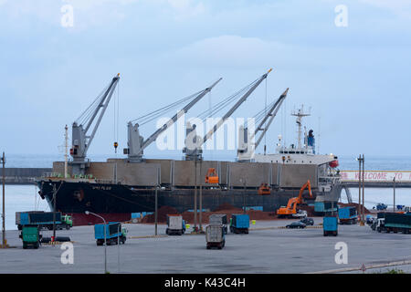 Uniplus bulk carrier cranes unloading loads with dump trucks waiting ...