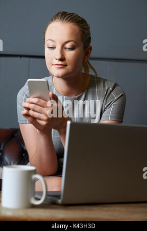 Businesswoman With Mobile Phone Working On Laptop In Internet Cafe Stock Photo