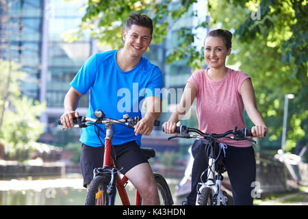 Young Couple Cycling Next To River In Urban Setting Stock Photo