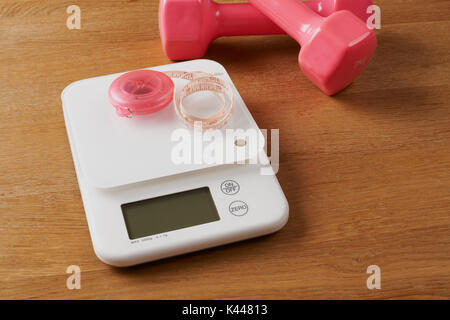 white food scales with pink tapeline and dumbbells on a wooden table Stock Photo