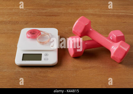 white food scales with pink tapeline and dumbbells on a wooden table Stock Photo