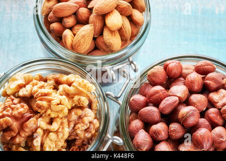 Walnuts, hazelnuts and almonds in jars on a rustic wooden background. Stock Photo