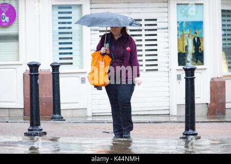 Woman walking holding a pink umbrella above her head to prevent rain falling on her along pavement in Chester City, Cheshire in pouring rain Stock Photo