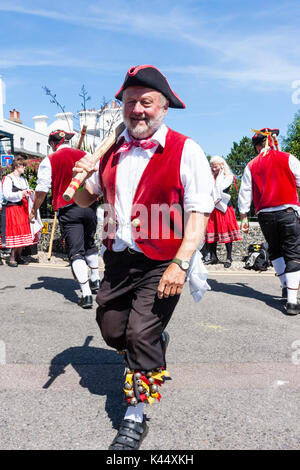 Traditional folk dancers, Victory Morris side, wearing 18th century sailor costume, red jack, black hat, holding wooden poles, dancing in the street. Stock Photo