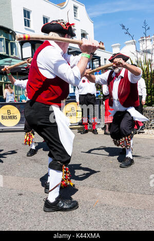 Traditional folk dancers, Victory Morris side, wearing 18th century sailor costume, red jack, black hat, holding wooden poles, dancing in the street. Stock Photo