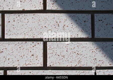 Close up of a wall highlighting a few white, speckled textured bricks and the dark cement between them. Stock Photo