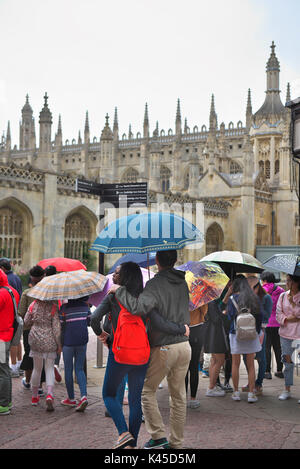 groups of foreign tourists with a tour guide gather outside Kings College in Cambridge with their colourful umbrellas Stock Photo