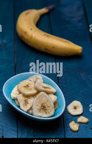 Dried banana in a bowl on petrol colored wooden background. Stock Photo