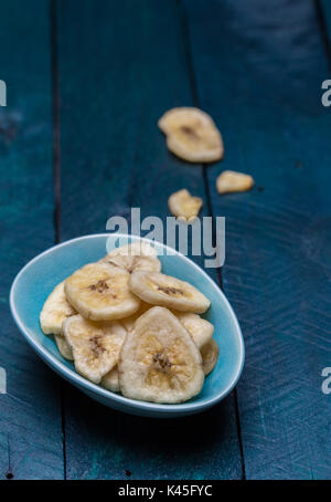 Dried banana in a bowl on petrol colored wooden background. Stock Photo