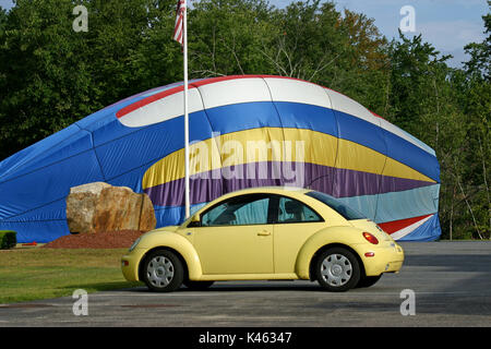 A 1999 yellow Volkswagen Beetle parked in front of a partially inflated, collapsing hot air balloon Stock Photo