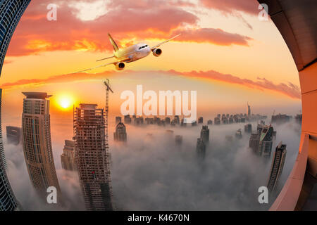 Plane is flying over Dubai against colorful sunset in United Arab Emirates Stock Photo