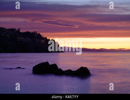 Beautiful dramatic sunset scenery in surreal pink colors on the Pacific ocean coast with lights of residential houses on dark rocky shores in Nanaimo,