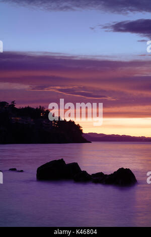 Beautiful pink sunset scenery on the ocean coast with lights of residential houses on dark rocky shores in Nanaimo, Vancouver Island, BC, Canada.