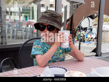 6 year old boy relaxing in a cafe in Stelvio with a hot chocolate after driving up the Stelvio Pass, sunglasses, hat and cool attitude Stock Photo