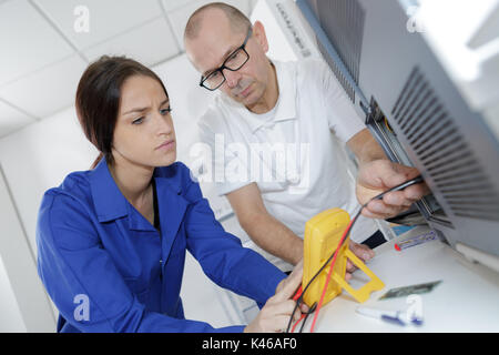 female electrician repairing a radiator helped by professor Stock Photo