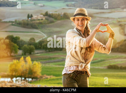 Discovering magical views of Tuscany. happy healthy woman hiker in hat in Tuscany showing heart shaped hands Stock Photo