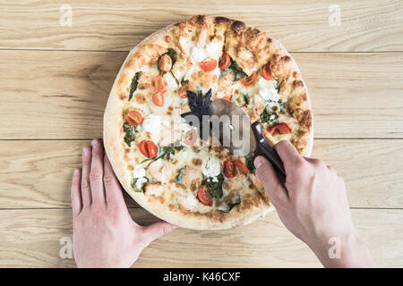 hands cutting italian pizza with wheel on wooden tabletop Stock Photo