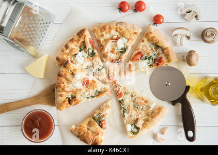 top view of sliced pizza with cheese and vegetables with kitchen utensils on tabletop Stock Photo