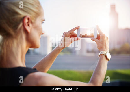 Portrait of mature woman taking a photo of cityscape by mobile phone. Stock Photo