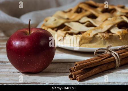 fresh apple and cinnamon sticks with homemade apple pie behind on wooden tabletop Stock Photo