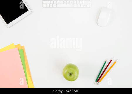 Top view of keyboard, computer mouse, digital tablet with blank screen, green apple and office supplies at workplace Stock Photo