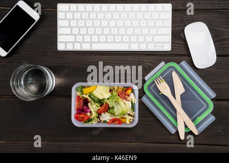 Top view of smartphone, computer keyboard and computer mouse with fresh salad on wooden table.  Stock Photo