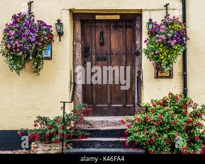 Old wooden front door surrounded by colourful flowers in Dunster High Street near Minehead, Somerset. Stock Photo
