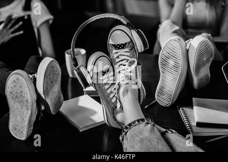 Close-up view of woman's feet in stylish shoes with headphones on wooden table, black and white photo Stock Photo